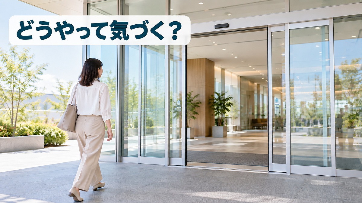 明るい建物の入口で、女性が近づくと中央から開くガラス製自動ドアと上部のセンサー